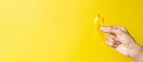 mano que muestra una cinta amarilla sobre fondo amarillo para apoyar a las personas que viven y están enfermas. día de prevención del suicidio de septiembre, mes de concientización sobre el cáncer infantil y concepto del día mundial contra el cáncer foto