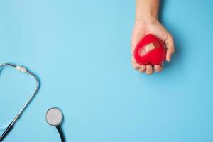 médico mano sosteniendo forma de corazón rojo con estetoscopio sobre fondo azul. cuidado de la salud, seguro de vida y concepto del día mundial del corazón foto