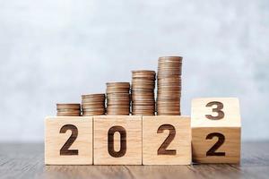 volteando el bloque de 2022 a 2023 años con pila de monedas. conceptos de dinero, presupuesto, impuestos, inversiones, finanzas, ahorros y resolución de año nuevo foto