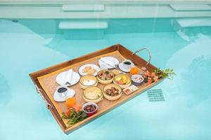 Floating Breakfast tray in swimming pool at luxury hotel or tropical resort villa, fruits, croissant, coffee, and orange juice. Exotic summer, relaxation, tropical travel and vacation concept photo