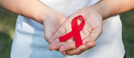 mano con cinta roja para apoyar a las personas que viven y están enfermas. concepto de salud y sexo seguro. diciembre día mundial del sida y mes de concientización sobre el cáncer de mieloma múltiple foto