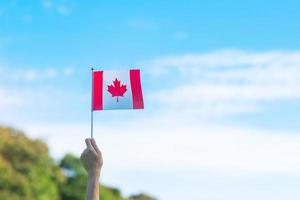 mano que sostiene la bandera de Canadá sobre fondo de cielo azul. canadá, día, y, feliz, celebración, conceptos foto