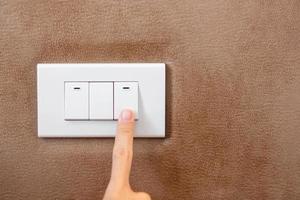 dedo encienda o apague el interruptor de luz en la pared en casa. conceptos de ahorro de energía, energía, electricidad y estilo de vida foto