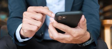 young Businessman in suit holding and using smartphone for sms messages, man typing touchscreen mobile phone in office or cafe. business, lifestyle, technology and Social media network concept photo