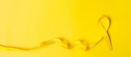 Yellow Ribbon on yellow background for supporting people living and illness. July Sarcoma cancer, Suicide prevention day, Childhood Cancer Awareness month concept photo
