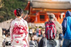 joven turista vistiendo kimono disfrutando con hojas coloridas en el templo kiyomizu dera, kyoto, japón. chica asiática con estilo de cabello en ropa tradicional japonesa en la temporada de follaje de otoño foto