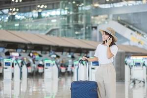 mujer joven que usa el teléfono inteligente y la mano que sostiene el asa del equipaje antes de verificar el tiempo de vuelo en el aeropuerto, transporte, seguros, viajes y conceptos de vacaciones foto