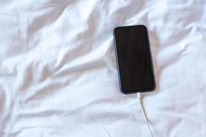 mobile smart phone charging battery on bed in the bedroom at home. Technology, multiple sharing and lifestyle concepts photo