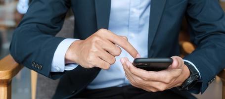 young Businessman in suit holding and using smartphone for sms messages, man typing touchscreen mobile phone in office or cafe. business, lifestyle, technology and Social media network concept photo