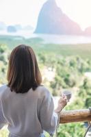 happy woman in bathrobe holding hot coffee cup or tea mug after waking up and enjoy Phang Nga bay view point, Tourist relaxing in tropical resort at Samet Nang She. Travel summer vacation concept photo