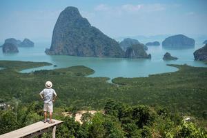 hombre viajero feliz disfruta del punto de vista de la bahía de phang nga, turista solo de pie y relajándose en samet nang she, cerca de phuket en el sur de tailandia. concepto de viaje, viaje y vacaciones de verano del sudeste asiático foto