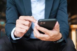 young Businessman in suit holding and using smartphone for sms messages, man typing touchscreen mobile phone in office or cafe. business, lifestyle, technology and Social media network concept photo