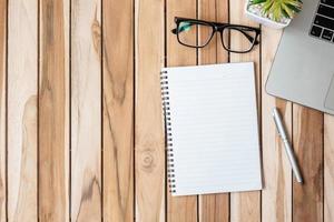 escritorio de oficina de vista superior con bolígrafo, computadora portátil y cuaderno en blanco sobre fondo de mesa de madera. espacio de trabajo u oficina en casa con espacio de copia para el concepto de texto foto