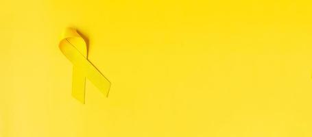 Yellow Ribbon on yellow background for supporting people living and illness. September Suicide prevention day, Childhood Cancer Awareness month and World cancer day concept photo