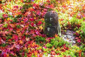 Japanese Jizo sculpture doll with falling Red Maple leaf in Japanese Garden at Enkoji Temple, Kyoto, Japan. Landmark and famous in Autumn season photo