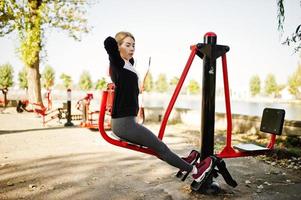 Young girl has the training and doing exercise outdoors on street simulators. Sport, fitness, street workout concept. photo