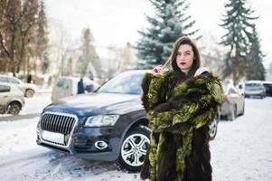 chica morena con abrigo de piel verde en la calle del coche de fondo de la ciudad en el día de invierno. foto