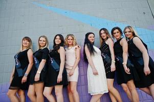 grupo de 8 chicas vestidas de negro y 2 novias en una despedida de soltera contra una pared colorida. foto