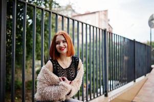 chica pelirroja con bolso rojo posado en un banco. foto