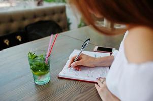 retrato de una hermosa y exitosa joven empresaria escribiendo algo en su cuaderno rojo mientras se sienta en un café. foto