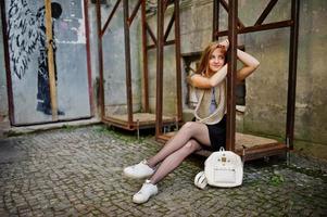 Young blonde girl in black skirt with scarf posed at street of city near the iron armor. photo