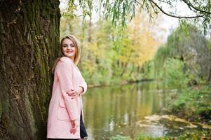 Young blonde girl at pink coat posed on autumn park. photo