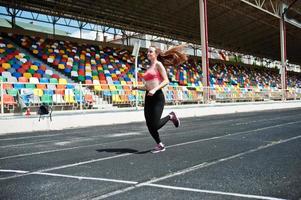 Fitness sporty girl in sportswear at stadium outdoor sports. Happy sexy woman running on athletic track treadmill on stadium. photo