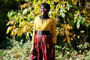 niña afroamericana en vestido amarillo y rojo en el parque de otoño. foto