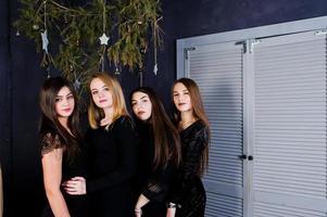 Four cute friends girls wear black dresses against christmas decoration. photo