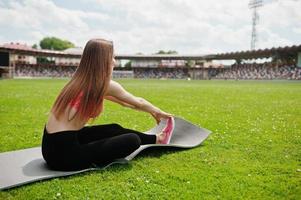 Fitness sporty girl in sportswear at a football stadium outdoor sports. Happy sexy woman workout on yoga mat background of green grass. photo