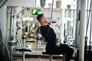 Muscular arab man training and doing workout on fitness machine in modern gym. photo