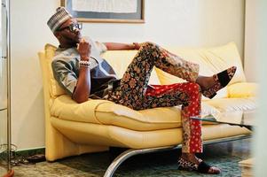 Rich african man sitting on sofa at his appartment. Portrait of successful black man indoor. photo