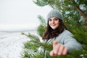 retrato de una chica gentil con abrigo gris y sombrero contra el árbol de año nuevo al aire libre. foto