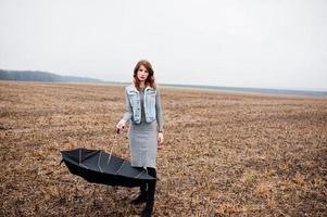 Portrait of brunette curly girl in jeans jacket with black umbrella at field. photo