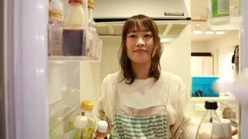 Eine Frau, die ein Smartphone hält und Zutaten aus dem Kühlschrank holt video