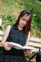 retrato de una mujer fabulosa con un vestido de lunares negros sentada en el banco y leyendo en el parque. foto