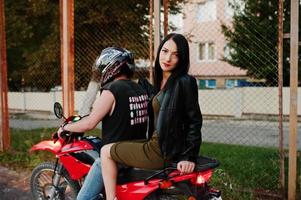 Woman in dress and leather jacket riding a motorbike with another man. photo