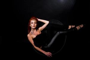 Fashion model red haired girl with originally make up like leopard predator isolated on black. Studio portrait on chair. photo