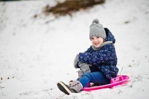 linda niña con trineos de platillos al aire libre en el día de invierno. foto