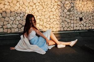 Portrait of an attractive young woman in blue dress sitting on the roof with white shawl. photo