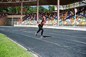 Fitness sporty girl in sportswear at stadium outdoor sports. Happy sexy woman running on athletic track treadmill on stadium. photo