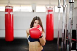 Young beautiful woman, wear on boxing gloves doing exercises and working hard in gym and enjoying her training process. photo
