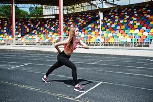 chica deportiva fitness en ropa deportiva en el estadio de deportes al aire libre. mujer sexy feliz corriendo en la caminadora de atletismo en el estadio. foto