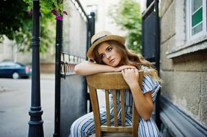 retrato de una mujer joven fabulosa en general a rayas y sombrero sentado y posando en la silla al aire libre. foto