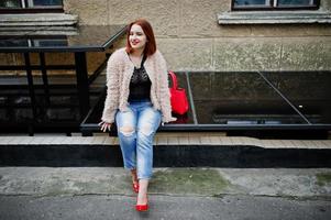 Red haired girl with red handbag posed at street of city. photo