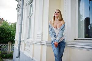 Blonde girl wear on jeans posed against old house. photo