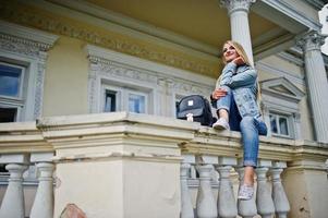 ropa de chica rubia en jeans con mochila posada contra casa vintage. foto