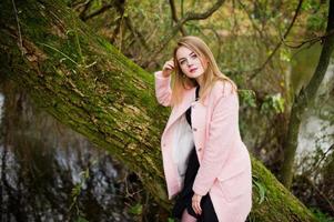 Young blonde girl at pink coat posed on autumn park. photo