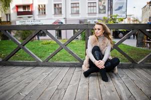 Blonde girl at fur coat sitting on wooden floor outdoor. photo