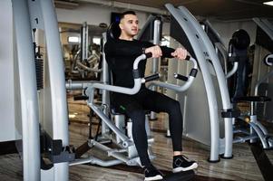 Muscular arab man training and doing workout on fitness machine in modern gym. photo